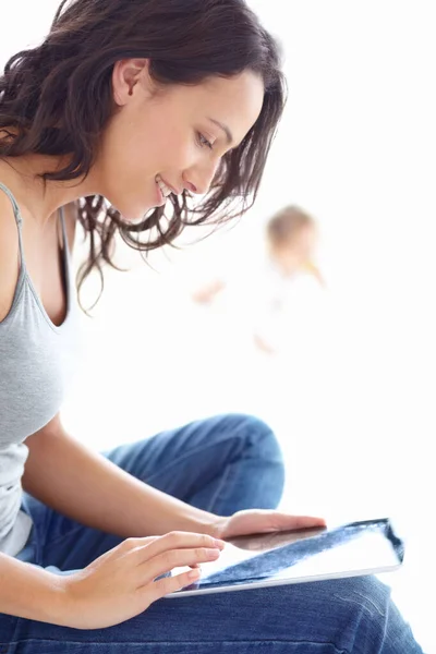 Liberdade digital para a nova mãe. Uma jovem mãe atraente trabalhando em seu tablet com seu bebê em segundo plano. — Fotografia de Stock