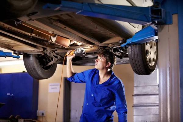 Jeg får lidt ekstra lys. En ung mandlig mekaniker ved hjælp af et lys til at kigge under en bil. - Stock-foto