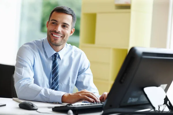 Travailler avec un sourire. Un jeune homme d'affaires souriant assis à son bureau et travaillant. — Photo