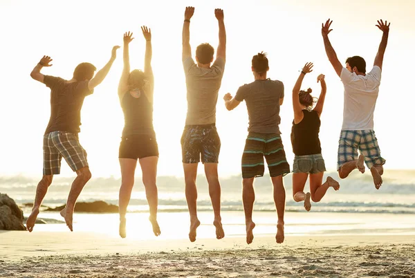 A apanhar ar na praia. Foto retrovisada de um grupo de amigos não identificáveis pulando juntos na praia ao pôr do sol. — Fotografia de Stock