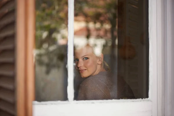 In a peaceful frame of mind. A young woman looking through her window. — Stock Photo, Image