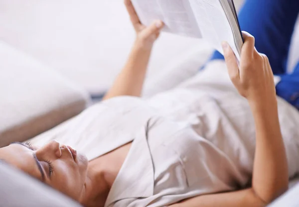 Dipende da ogni parola. Girato di una giovane donna che legge un romanzo sdraiata su un divano. — Foto Stock