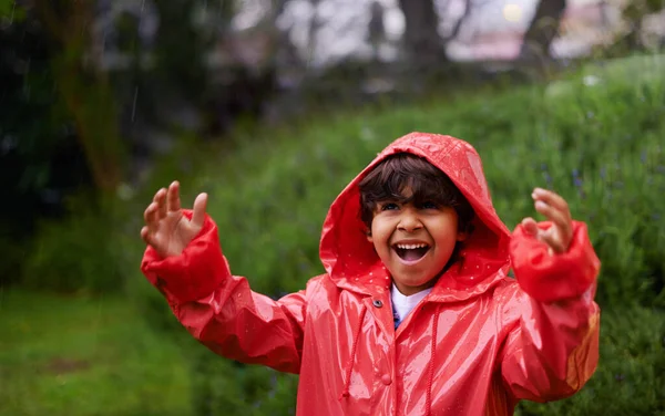 Ele está a cantar à chuva. Tiro de um menino vestindo uma capa de chuva brincando lá fora. — Fotografia de Stock