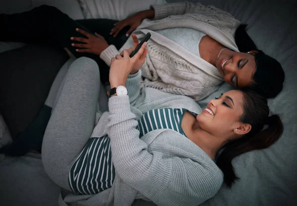 Lassen Sie mich Ihnen dies zeigen... Schnappschuss von zwei jungen Frauen, die etwas auf einem Handy betrachten, während sie auf einem Bett liegen. — Stockfoto