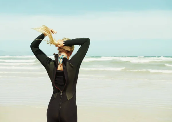 Ihre Haare zum Trost beim Surfen zurückbinden. Ein Surfermädchen, das seine Haare zu einem Pferdeschwanz bindet. — Stockfoto