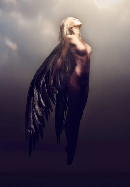 Watch her feminine splendor take flight. Shot of a gorgeous woman with feathered wings in a fantasy-like setting. — Stock Photo, Image