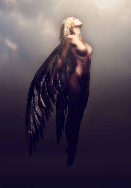 Shot of a gorgeous woman with feathered wings in a fantasy-like setting.
