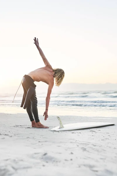 Wszystko gotowe do podboju oceanu. Full length shot przystojnego młodzieńca rozciągającego się przed udaniem się na surfing na plaży. — Zdjęcie stockowe