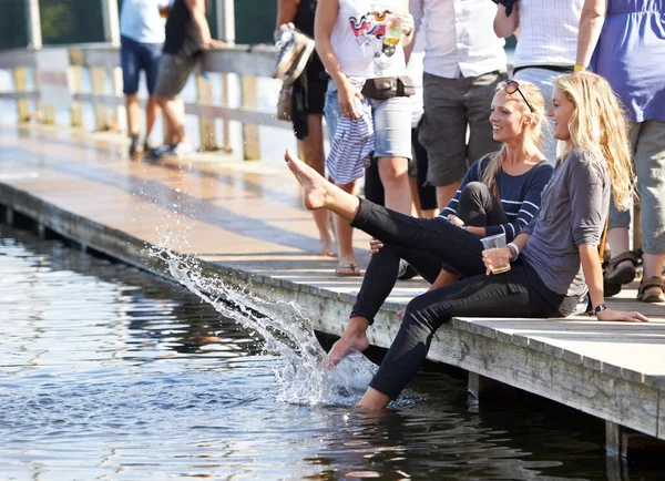 Dándoles a sus pies un merecido descanso. Fotografía de dos jóvenes sentadas con los pies en el agua en un festival al aire libre. — Foto de Stock