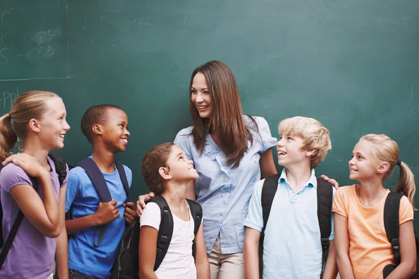 Tworzy szczęśliwą klasę. Piękna młoda nauczycielka stojąca ze swoją klasą przy tablicy i uśmiechnięta. — Zdjęcie stockowe