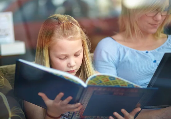 Lezen oefent de hersenen. Een schattig jong meisje zit naast haar moeder terwijl ze een boek lezen. — Stockfoto