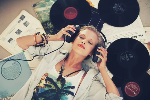 Zachowaj spokój i pozwól grać muzyce. Młoda kobieta słuchająca muzyki leżąc na plecach i otoczona płytami. — Zdjęcie stockowe