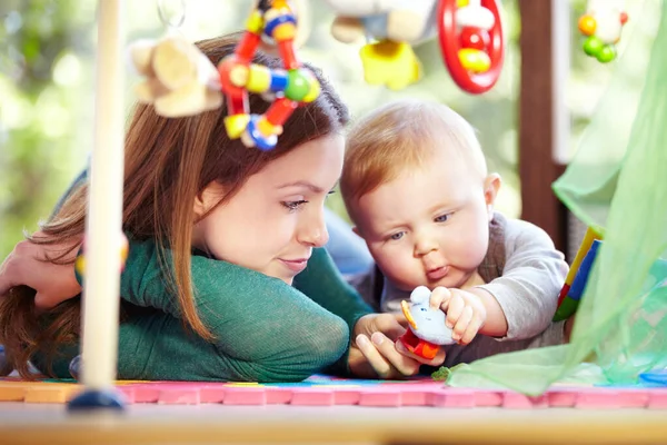 Voller Neugier. Süße junge Mutter liegt neben ihrem kleinen Sohn auf dem Fußboden des Spielzimmers. — Stockfoto