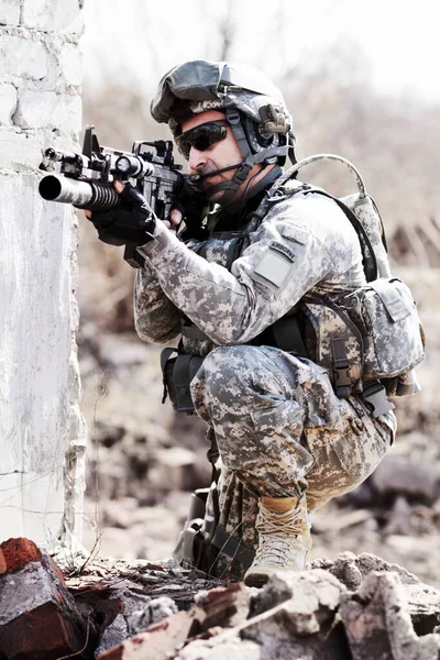 领导这个无赖。一个士兵蹲伏在倒塌的墙边，用枪指着远方. — 图库照片