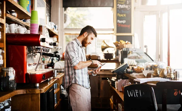Technology makes it so easy to multitask. Shot of a young man using a digital tablet while working in a coffee shop. — Stock Photo, Image