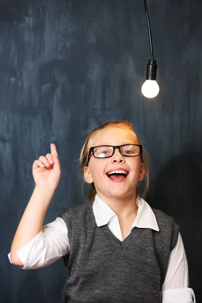 Shes full of bright ideas. A cute blonde girl getting an idea below a lightbulb in class. — Stock Photo, Image