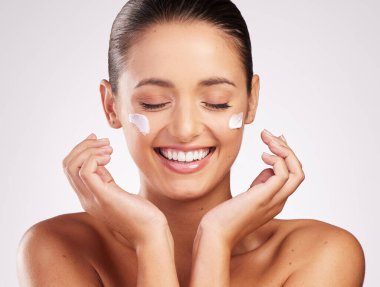 So hydrated you can feel how happy your skin is. Shot of an attractive young woman applying moisturiser to her face against a studio background. clipart