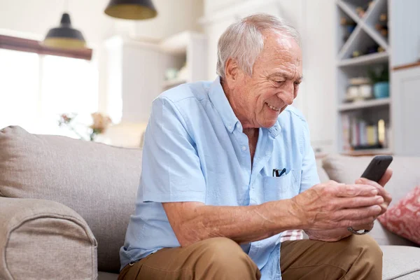 Olha para aquilo... Tiro de um homem idoso olhando feliz ao usar seu smartphone em casa no sofá. — Fotografia de Stock