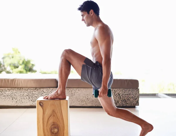 La aptitud se trata del compromiso diario. Un joven musculoso haciendo ejercicios de fuerza con pesas en casa. —  Fotos de Stock