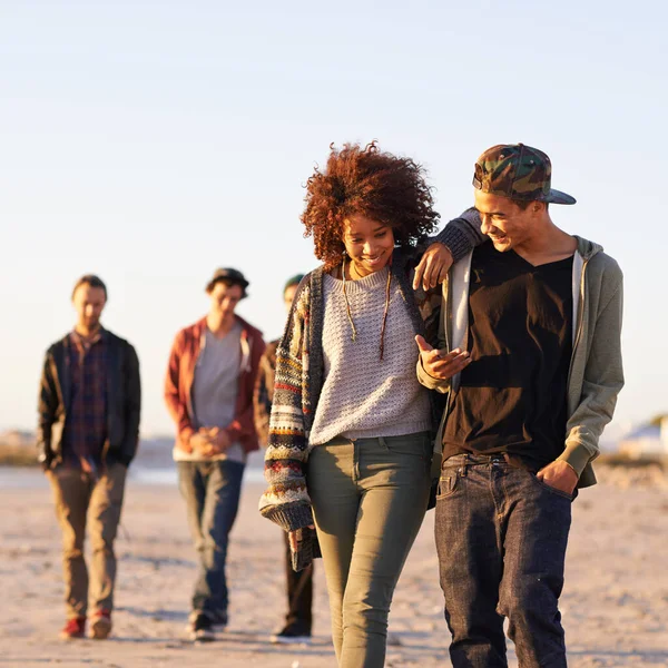 Ze heeft iets over haar. Opname van een groep vrienden die bij zonsondergang langs een strand lopen. — Stockfoto