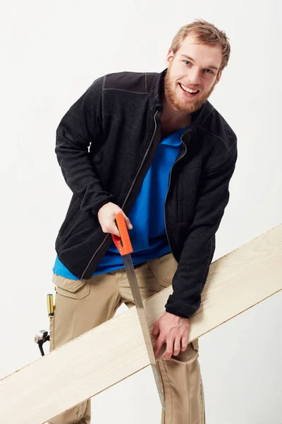 Casual carpenter. Portrait of a young carpenter sawing a piece of wood against his leg. — Stock Photo, Image