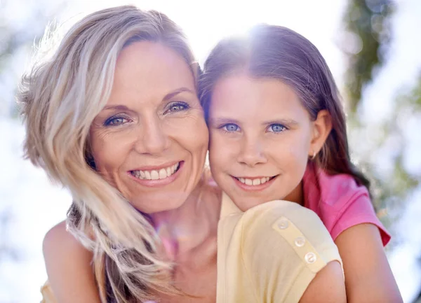 Egyforma mosoly. Egy mosolygó anya a lányával a hátán, miközben a szabadban van.. — Stock Fotó