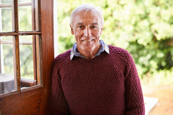 Invite an old man inside. Portrait of a happy senior man leaning against the doorway to his home.