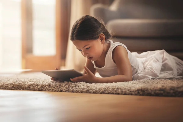 Oktatási alkalmazások az ujjai köré csavarták. Egy imádnivaló kislányról készült felvétel, aki digitális tabletet használ otthon a padlón.. — Stock Fotó