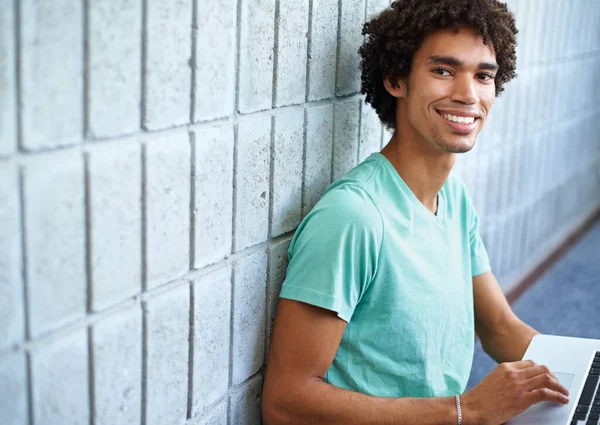 Bezdrátový internet dělá z výzkumu vánek. Mladý muž používající svůj notebook a usmívající se do kamery. — Stock fotografie