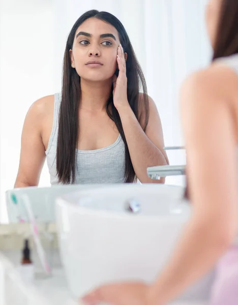 Hm my skin has been absolutely glowing lately. Shot of a young woman admiring her skin in her bathroom mirror. — Stock Photo, Image