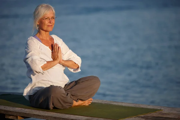 Lugn vid havet. Skjuten av en attraktiv mogen kvinna som gör yoga på en pir ute på havet. — Stockfoto