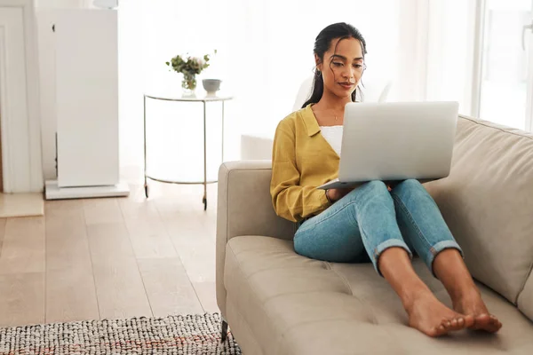 Den Tag mit einer Aufgabe nach der anderen überstehen. Ganzkörperaufnahme einer attraktiven jungen Geschäftsfrau, die zu Hause auf ihrer Couch sitzt und von ihrem Laptop aus bloggt. — Stockfoto