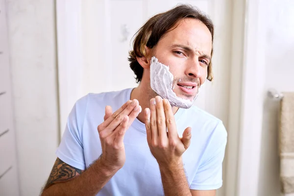 Trying out a new shaving foam is always dicey. Shot of a young man applying shaving foam to his face. — Stock Photo, Image