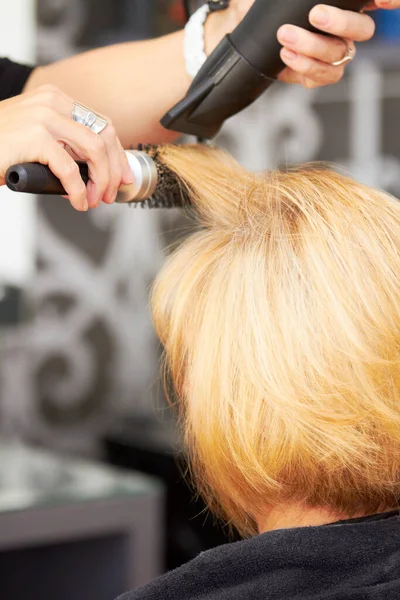 Doskonalenie każdego kosmyka włosów. Blondynka suszy włosy u fryzjera. — Zdjęcie stockowe