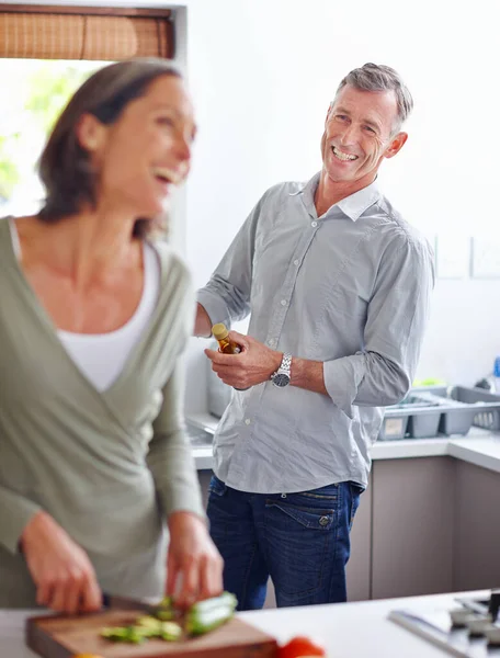 Making each other laugh. Shot of a mature couple laughing while preparing a meal together in the kitchen. — Stock Photo, Image