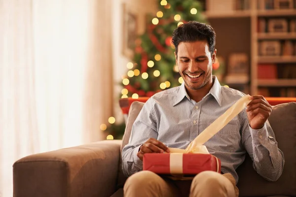 Sich an Weihnachten wie ein Kind fühlen. Aufnahme eines gutaussehenden jungen Mannes beim Öffnen eines Weihnachtsgeschenks. — Stockfoto