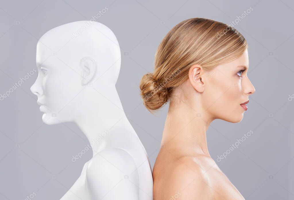 Real vs artificial beauty. A beautiful young woman standing back to back with a mannequin.