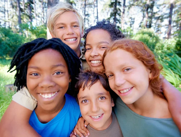 Kul, vänner och frisk luft. En närbild av en grupp barn som ler mot kameran när de står i skogen. — Stockfoto