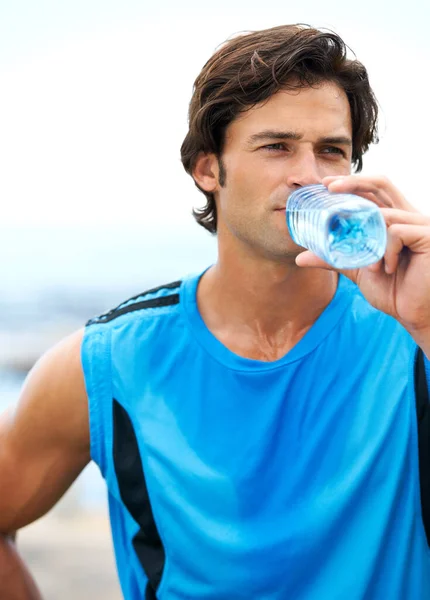 Asegúrese de beber suficiente agua durante el entrenamiento. Un hombre joven y apto bebiendo agua de una botella de agua durante su rutina de ejercicios matutinos. — Foto de Stock