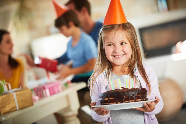 Algo dulce para celebrar los ocho años. Foto de una niña feliz sosteniendo un pastel de cumpleaños con su familia en el fondo. —  Fotos de Stock