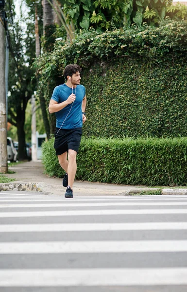 Es seguro cruzar. Foto de un joven deportivo corriendo a través de una carretera como ejercicio al aire libre durante el día. — Foto de Stock