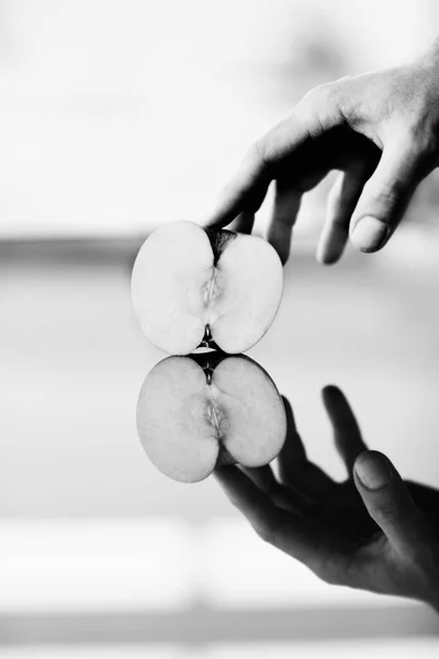 Réfléchir sur la santé. Une main tenant la moitié d'une pomme contre une surface brillante avec son reflet en dessous. — Photo