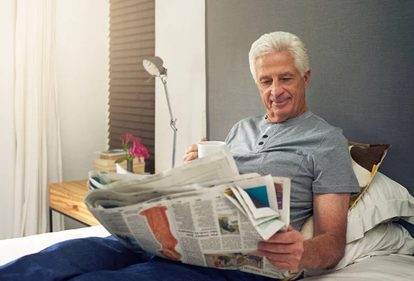 Encuentra satisfacción en la lectura de la buena escritura. Foto de un hombre mayor leyendo el periódico en la cama mientras tomaba café. —  Fotos de Stock