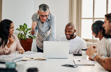 Sonunda tasarımlarını internette gördüğünde. Modern bir ofiste toplantı sırasında dizüstü bilgisayar kullanırken tezahürat yapan bir grup iş adamının fotoğrafı..