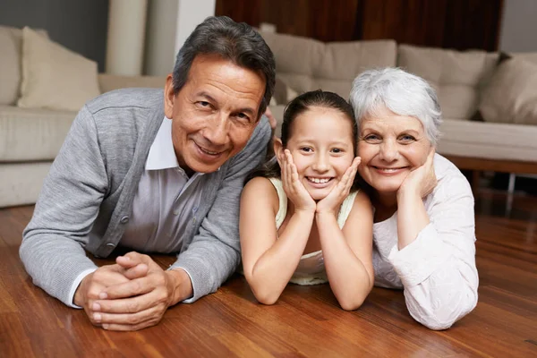 Divertimento sul pavimento con la nonna e il nonno. Una ragazza sdraiata e sorridente alla telecamera con i nonni. — Foto Stock