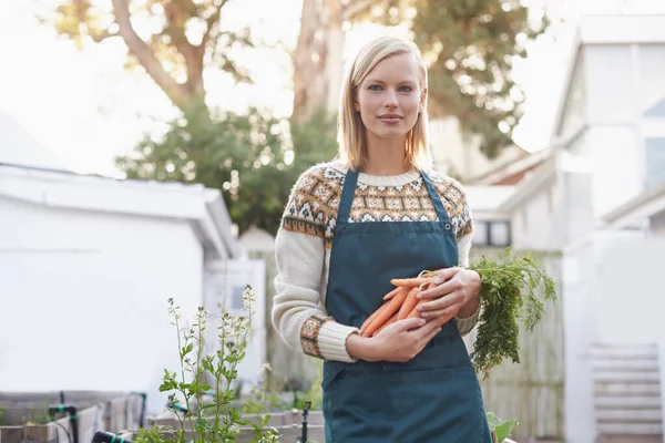 Organic gardening. A young woman holding carrots in her garden. — Stock Photo, Image