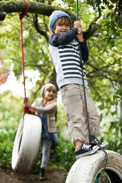 命を振り払う。2人のかわいい子供のショット彼らの庭でタイヤのスイングで遊ぶ. — ストック写真