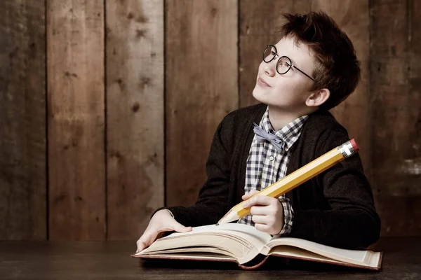 Leírok néhány nagy ötletet. Fiatal fiú szemüveget visel és egy hatalmas ceruzával csinálja a házi feladatát.. — Stock Fotó