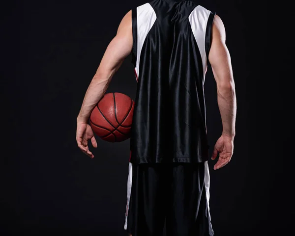 Los ganadores nunca renuncian y los que renuncian nunca ganan. Vista trasera recortada de un jugador de baloncesto sosteniendo una pelota de baloncesto sobre un fondo negro. — Foto de Stock