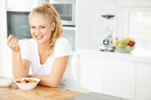 Ha un sapore fantastico. Attraente giovane donna mangiare macedonia di frutta nella sua cucina. — Foto Stock